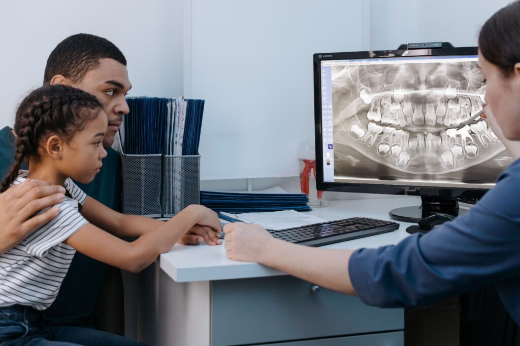Pediatric dentist explaining a child's oral health during a routine dental exam with a parent present.